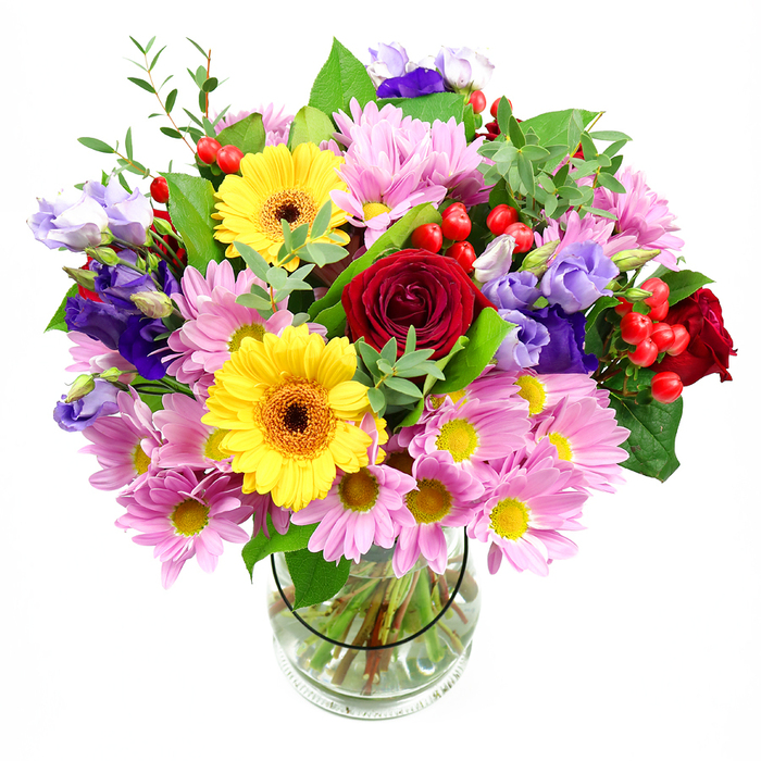 This photograph captures a lush, thoughtfully composed bouquet presented in a clear glass vase, silhouetted against a crisp white backdrop that throws the colours into sharp relief. At the heart of the display, several deep red roses command attention, their petals velvety and tightly layered, giving a sense of depth, passion, and timeless elegance. Immediately beside them, two yellow gerbera daisies with dark, warm-toned centres shine like small suns, their broad, flat petals radiating outwards and infusing the arrangement with a joyful, celebratory tone. Flowing out from this central cluster, generous groups of soft pink daisies or chrysanthemums spill gently, each bloom composed of fine, feathery petals around a small yellow centre, creating a soft cushion of pastel colour that adds both volume and tenderness. Between these pastel flowers, stems of lisianthus in rich purple and softer lavender tones curl and bend, their slightly ruffled, bell-shaped blossoms introducing cool highlights and elegant movement, much like the shifting light over nearby Byfleet and New Haw. Scattered artfully among the petals, bright red hypericum berries form rounded clusters, their glossy surfaces catching the light and contributing a playful, textured element. The bouquet is embraced by a collar of mixed greenery, from deep, broad leaves that anchor the base to lighter, slender sprigs that arch upwards, giving the whole piece a fresh, garden-like character reminiscent of local Byfleet gardens after a summer rain. Inside the clear glass vase, the neatly trimmed stems fan into clean water, emphasizing the care, skill, and freshness behind the arrangement. The mood is uplifting, warm, and versatile, ideal for birthdays, congratulations, or simply bringing a burst of colour and life into a Byfleet home, café, or office space.